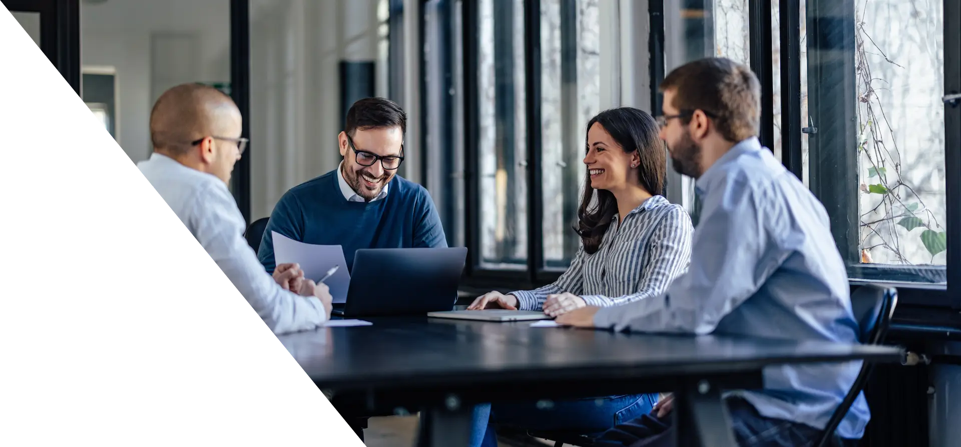 three people sitting at a table with laptops and papers