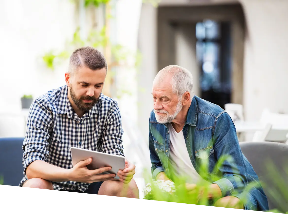 two men sitting on a couch looking at a tablet computer